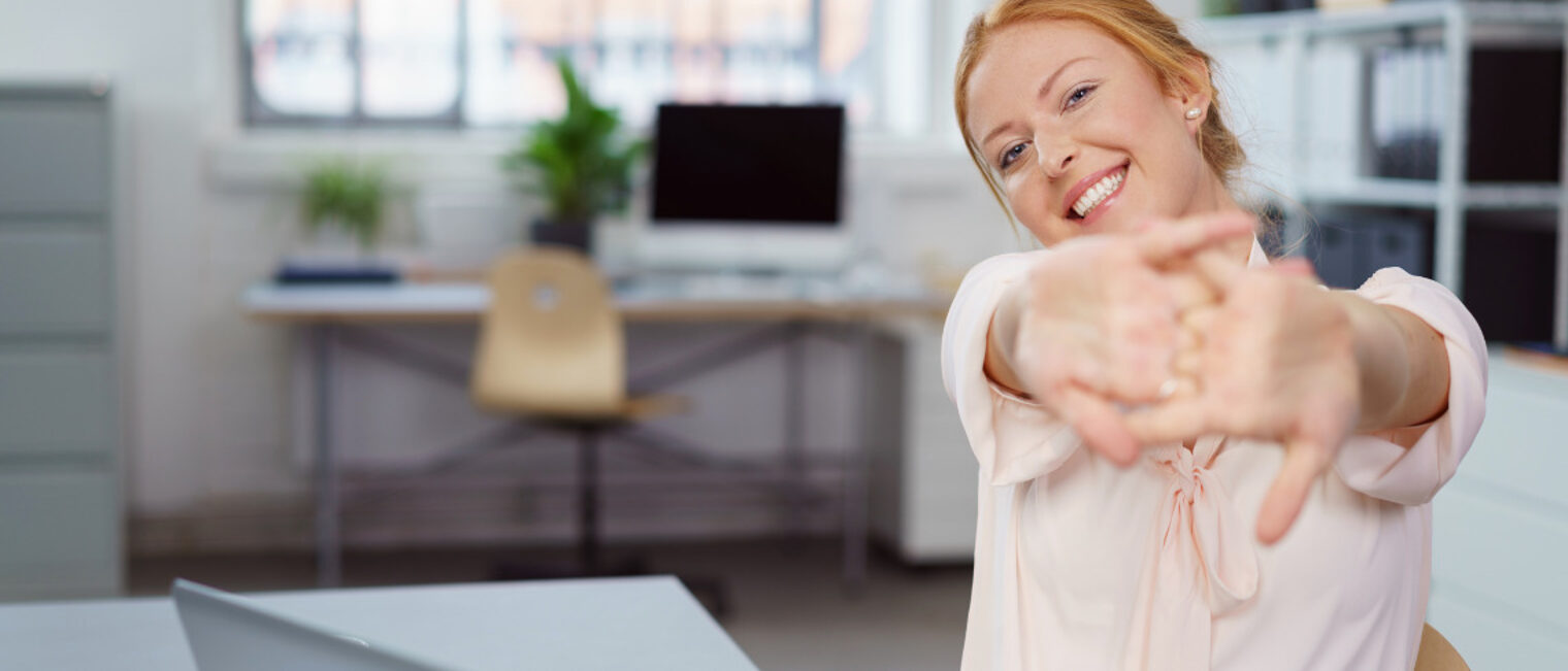 Frau im Büro am Tisch dehnt ihre Hände und Arme.