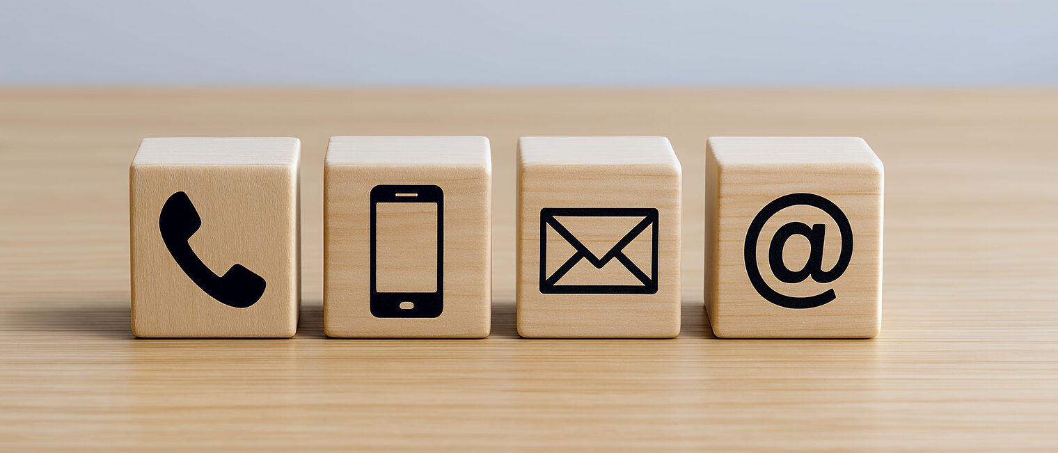Vier Holzwürfel auf einer Platte mit den Symbolen Telefon, Handy, Briefumschlag und @-Zeichen.