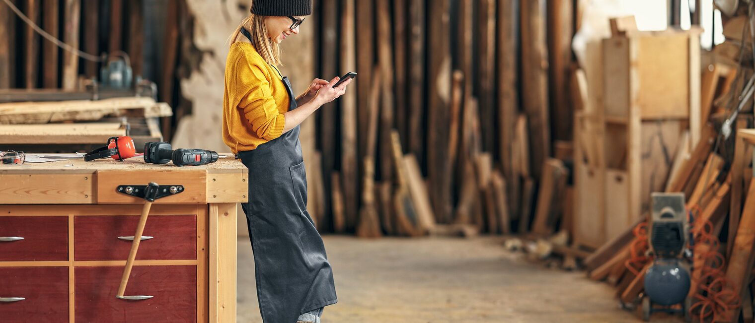 Frau mit Handy in einer Werkstatt.