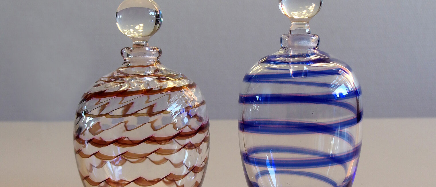 Zwei Parfümfläschchen aus Glas, eine mit roten Linien, eine mit blauen.