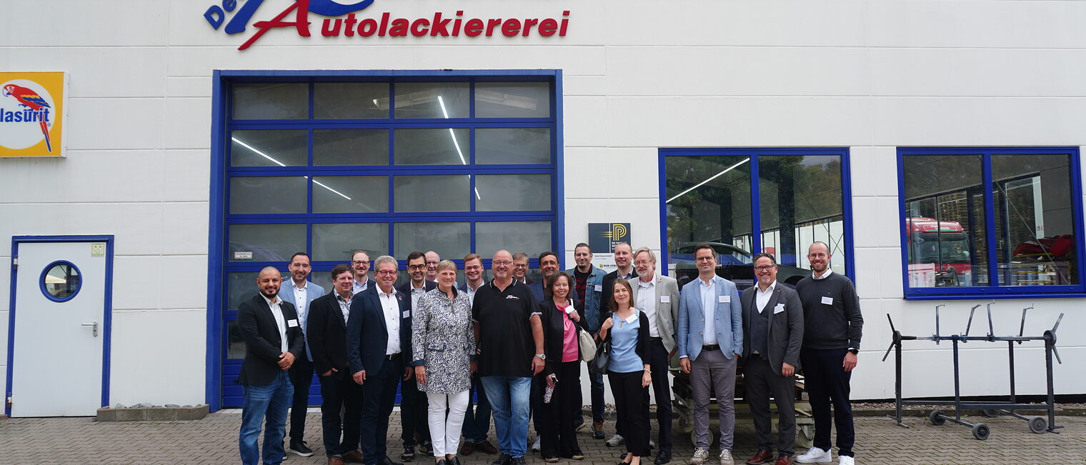 Gruppe steht vor einem großen Hallenstor der Autolackierer Rauhut.