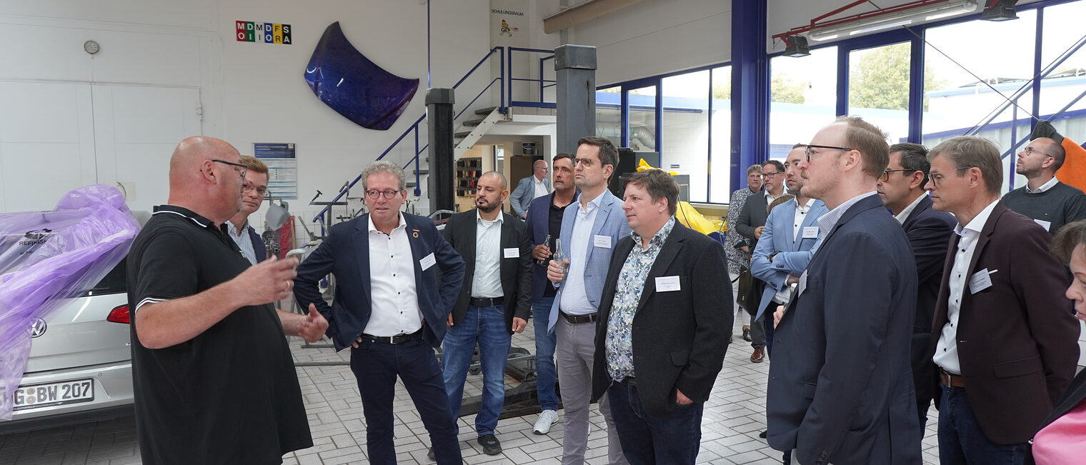 Inhaber spricht in einer Werkstatt vor der Besuchsgruppe.