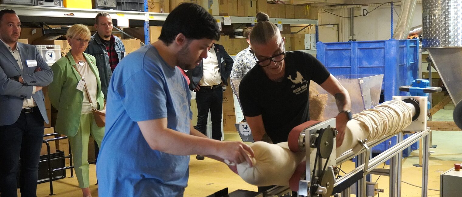 Zwei Männer führe an einer Machine vor, wie die Haarschläuche befüllt werden.